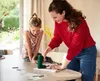A woman and a child are at a table, working on a project with a power tool. Produktbild-Vorschau