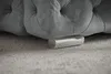 A close-up view of the bottom of a tufted upholstered bed frame, showing one of its metallic feet resting on a textured carpet. Náhľad obrázku produktu