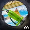 A man is holding a green submersible pump while looking out of a dark opening. Podgląd zdjęcia produktu