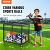 A boy is holding a ball next to a metal ball storage cage filled with sports balls on a green field. Produktbild-Vorschau