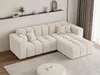 A cream-colored sectional sofa is arranged in a living room setting, with a round white coffee table in front and a shelf with decorative items behind it. Produktbild-Vorschau