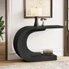 A black C-shaped console table with a lamp and vase on top, and books on the lower shelf, placed in a hallway with a rug and a plant. Anteprima dell’immagine prodotto