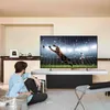 A man is sitting on the floor watching a soccer game on a large TV screen. Voir les images du produit