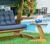 A wooden swing chair with a blue cushion is placed on a green lawn next to a swimming pool. A small wooden table with a blue vase of flowers and a book is next to the chair. Podgląd zdjęcia produktu