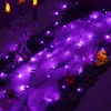 A Halloween-themed table runner decorated with purple LED string lights, fake cobwebs, a skull, and a small pumpkin. Produktbild-Vorschau