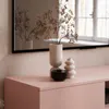 A pink TV cabinet with decorative items on top, including vases and a bowl, with a mirror reflecting the scene in the background. Produktbild-Vorschau