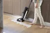 A person is using a wet/dry vacuum cleaner to clean up a spill on a wooden floor in a kitchen or utility room. Náhled obrázku produktu