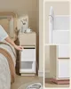 A person's hand is reaching into a modern, narrow nightstand next to a bed. Náhled obrázku produktu