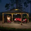An outdoor patio scene at dusk, featuring a wooden gazebo with furniture and a fireplace. Náhled obrázku produktu