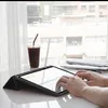 Hands typing on a tablet with a coffee cup and papers on a desk by a window. Podgląd zdjęcia produktu