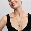 A woman wearing a black top and gold jewelry, smiling. Produktbild-Vorschau
