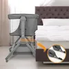 A baby bassinet is placed next to a bed, with straps shown to secure it to the bed. Produktbild-Vorschau