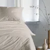 A close-up view of a bed with beige bedding, next to a window with a vase of branches. Produktbild-Vorschau