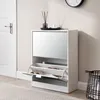 A white shoe cabinet with a mirrored front is shown in a room with a white door and a rug. Náhľad obrázku produktu