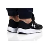 A close-up shot of a person wearing black Under Armour sneakers with white soles. Produktbild-Vorschau