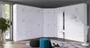 A large, white, high-gloss corner wardrobe with multiple doors and drawers, set up in a room with a window and decorative elements. Náhled obrázku produktu