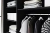 A close-up view of a wardrobe interior, showing shelves with folded clothes and a hanging rail with several garments. Produktbild-Vorschau