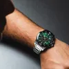A close-up shot of a man's arm wearing a green-faced chronograph watch. Náhled obrázku produktu