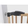 A close-up view of a safety gate mounting bracket attached to a wooden railing and a white wall. Podgląd zdjęcia produktu