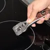A hand is using a scraper tool on a black glass stovetop. Podgląd zdjęcia produktu