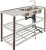A stainless steel double sink with a faucet and drain assembly, shown on a white background with a metal shelving unit underneath. Náhled obrázku produktu