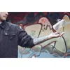 A person's arm and hand are shown levitating a Bluetooth speaker in front of a graffiti-covered wall. Anteprima dell’immagine prodotto