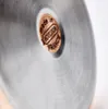A close-up of the bottom of a pot or pan, showing a circular metal emblem with text. Produktbild-Vorschau
