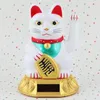 A white Maneki-neko (lucky cat) figurine with red ears and collar, holding a gold coin, sits on a gold solar-powered base against a patterned background. Produktbild-Vorschau