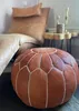 A close-up shot of a Moroccan leather pouf in a living room setting, with a chair and side table in the background. Podgląd zdjęcia produktu