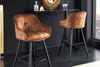 Two brown bar stools are placed in a modern, dimly lit room with a black wall and a bar in the background. Produktbild-Vorschau