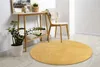 A round yellow rug is placed on a light wooden floor in a room with a console table and a chair. Produktbild-Vorschau
