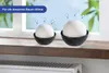 Two white spheres in black bowls on a windowsill, with a radiator below and a window behind. Produktbild-Vorschau