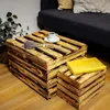 A wooden crate coffee table and a smaller matching crate are placed on a wooden floor in front of a sofa. A cup of coffee, a small bunch of lavender, and a yellow book are on top of the coffee table. Produktbild-Vorschau