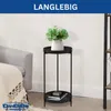 A black metal plant stand with two tiers, holding a potted plant and some books, next to a grey sofa with a cream blanket. Podgląd zdjęcia produktu