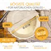 A close-up shot of a round rattan bread proofing basket with a linen liner, set on a wooden surface with some flour scattered around. Various marketing text overlays highlight product features and quality. Produktbild-Vorschau