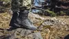 A person wearing camouflage pants and black boots stands on rocks in a natural outdoor setting. Produktbild-Vorschau