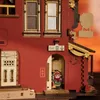 A close-up of a wooden model of a building with a small character figure peeking out of an open doorway. Podgląd zdjęcia produktu