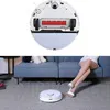 A robot vacuum cleaner is shown from above and in use on a carpet next to a sofa where a person is sitting. Produktbild-Vorschau