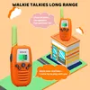 Two orange and green walkie-talkies are shown, one in the foreground and one on top of a cartoon building. There are speech bubbles with text. Náhľad obrázku produktu