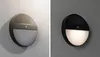 Two images of a solar-powered outdoor wall light mounted on a textured wall. The left image shows the light in daylight, and the right image shows it illuminated at night. Náhled obrázku produktu