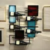 A modern metal wine rack mounted on a wall, holding several bottles of wine. The rack has a geometric design with colored rectangular accents. Náhled obrázku produktu