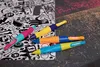 Four colorful ergonomic pens are arranged on a surface with a patterned background. Anteprima dell’immagine prodotto