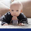 A baby is lying on a bed and drinking from a sippy cup. Produktbild-Vorschau