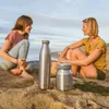 Two women sitting on a beach with two stainless steel bottles. Náhled obrázku produktu