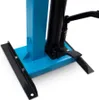 A close-up view of the base of a hydraulic spring compressor, showing the blue base plate, black pedals, and a black hydraulic cylinder. Produktbild-Vorschau
