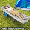 A woman is relaxing on a padded camping cot next to a tent in a grassy area. Podgląd zdjęcia produktu