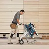 A man is pushing a Bosch table saw on a stand with wheels. Voir les images du produit