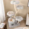 A multi-level cat tree with plush lounging platforms and a cat cave, set in a room with light-colored walls and a window with sheer curtains. Podgląd zdjęcia produktu