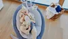 A baby is lying in a baby bouncer with toys hanging above. Produktbild-Vorschau
