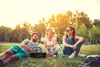 Three people are sitting on the grass in a park, with a stereoradio in the foreground. Produktbild-Vorschau